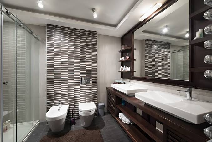Baño moderno con azulejos a rayas, dos lavabos dobles, espejo grande y ducha de vidrio.